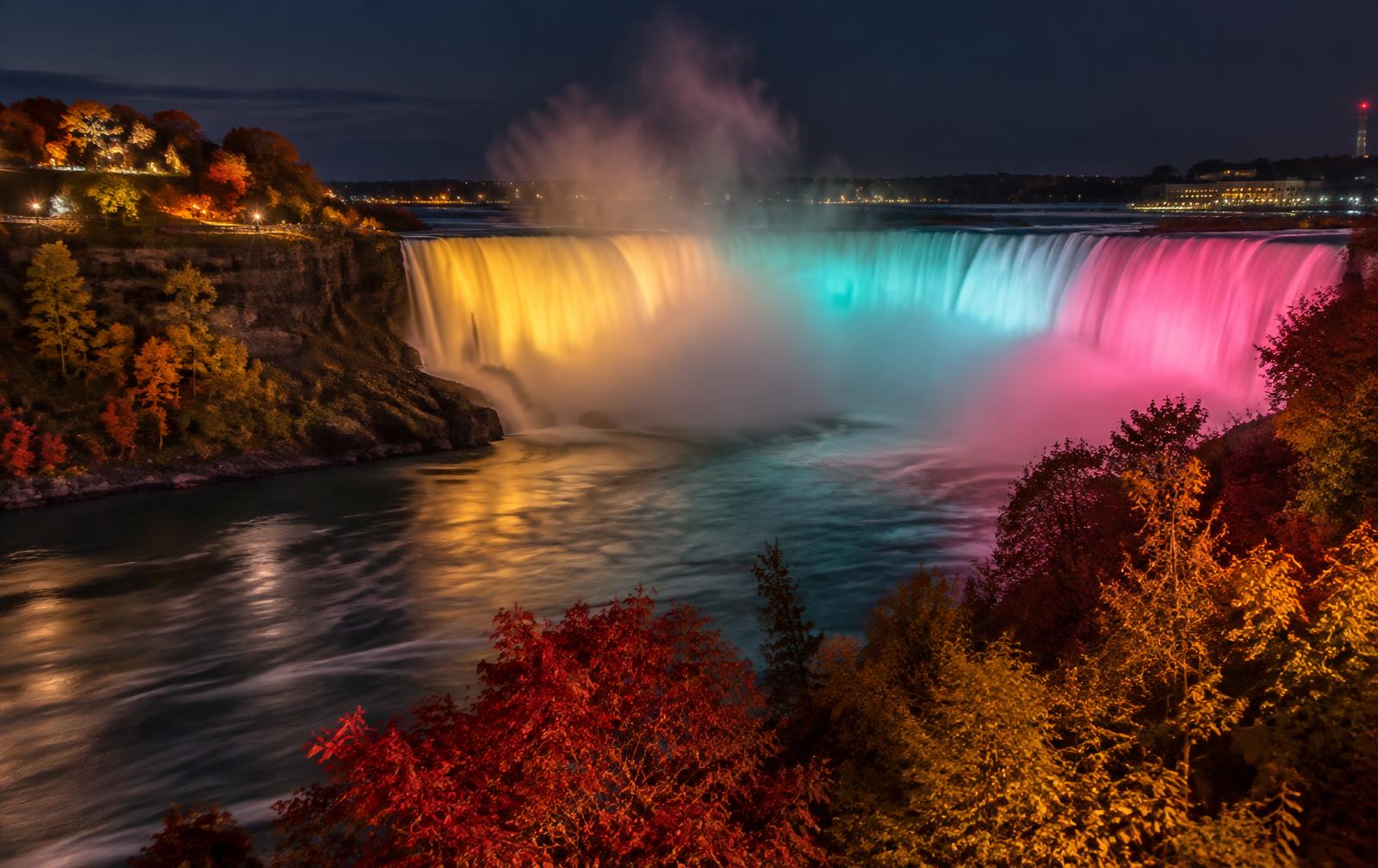 The illuminated Horseshoe Falls at night in autumn, festival lights on the water and warm fall colours on the trees